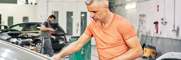 Mechanic in orange shirt works on a car